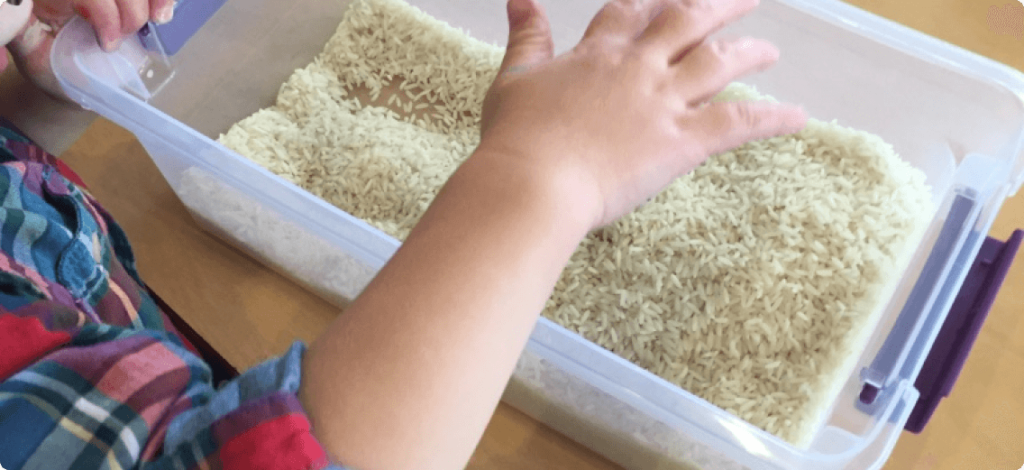 a child happily playing with rice in a plastic container