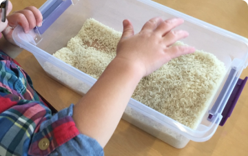 a child happily playing with rice in a plastic container thumbnail