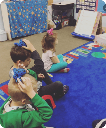 a group of children on the classroom floor, focused on their tasks, all with their hair styled in neat ties
